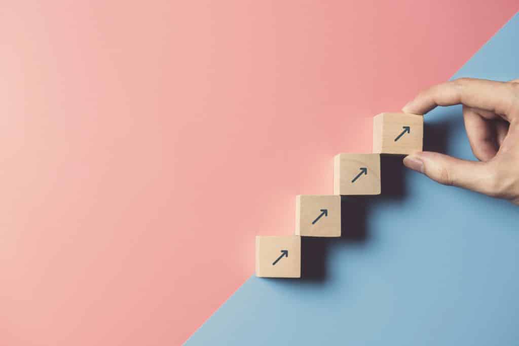 Business concept growth success process, Close up man hand arranging wood block stacking as step stair on paper blue and pink background, copy space.